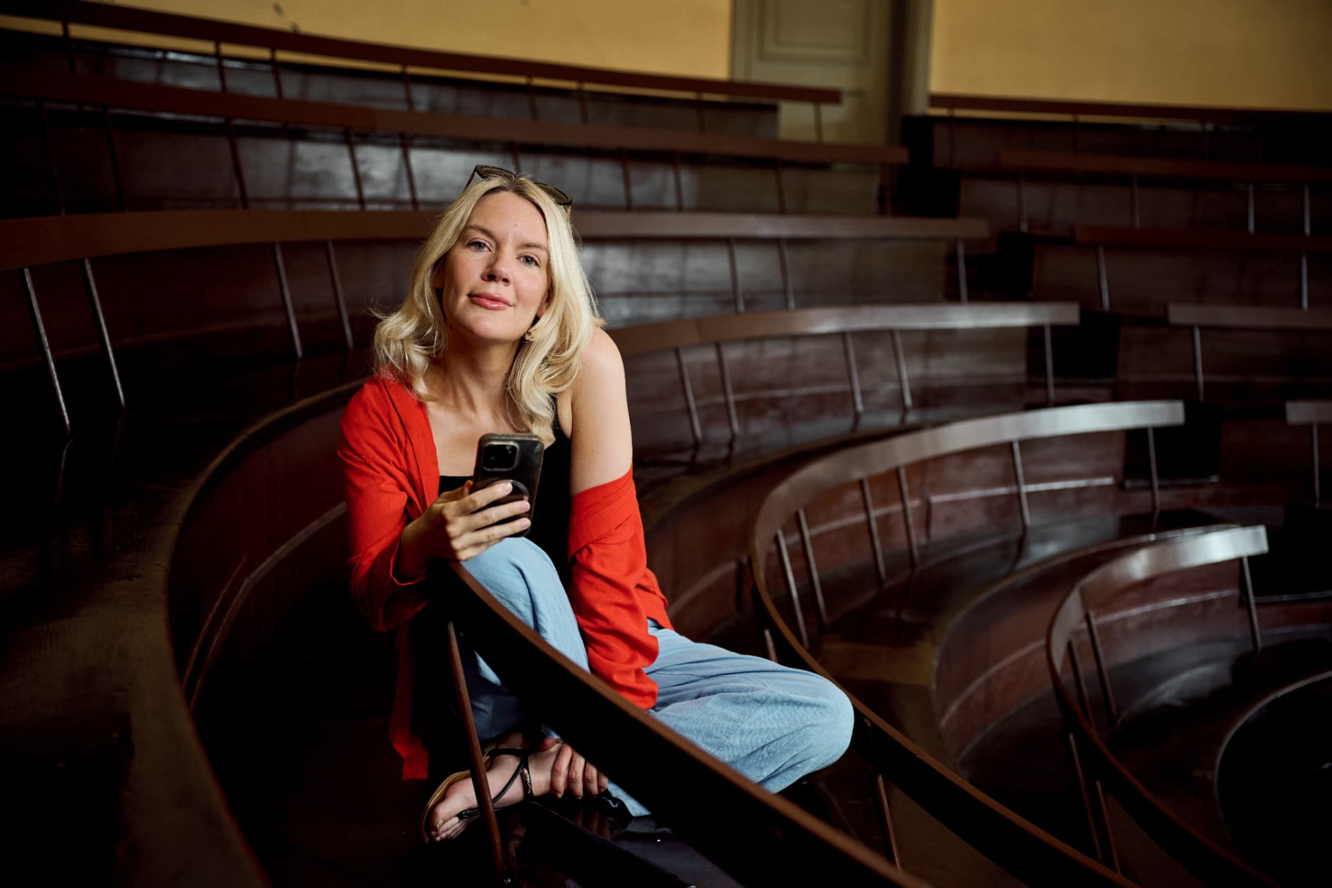Lægen Amanda Palbo sidder med sin telefon i et gammelt auditorium